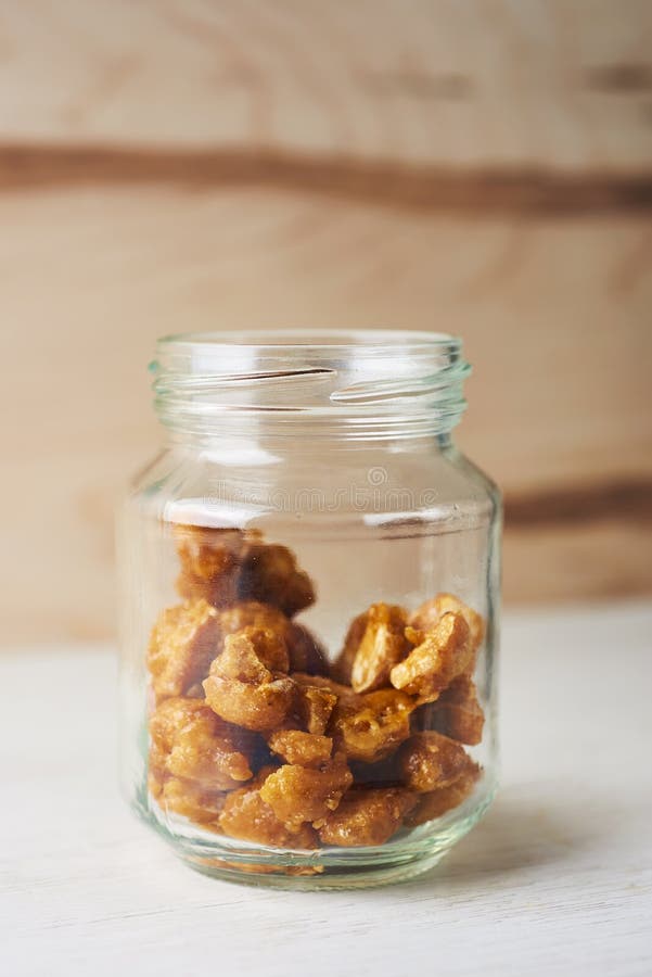 Closeup of some nueces de macadamia garrapinadas, spanish candied macadamia nuts, in a glass jar on a wooden table