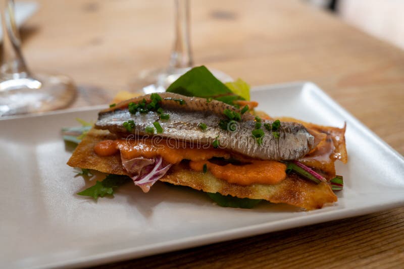 Spanish food, one tapas small piece of roasted bread cracker with vegetables puree and smoked sardine fish