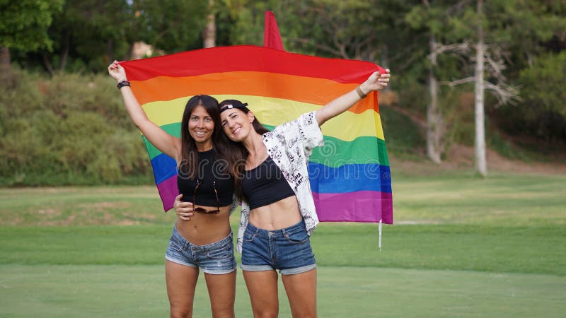 Spanish Lesbian Couple Posing In A Golf Field With A Pride Flag Stock