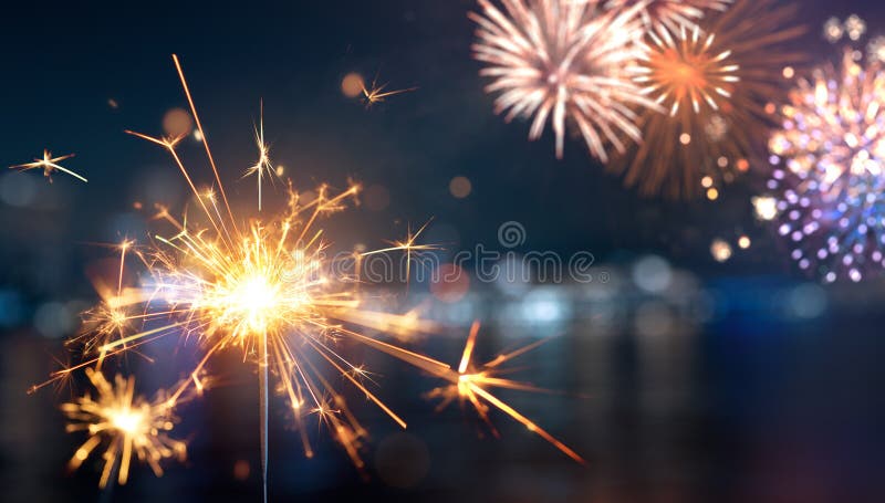 Sparkler with blurred fireworks light up the night sky royalty free stock image