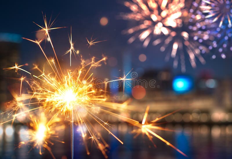 Sparkler with blurred fireworks light up the night sky stock photo