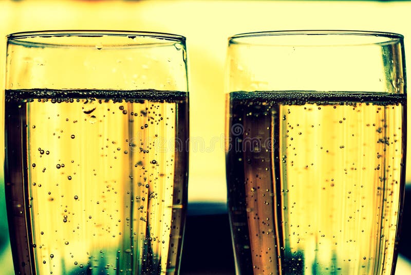 Side view of sparkling wine in glasses with yellow background.