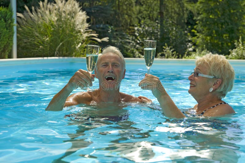 Felice coppia di anziani divertirsi bevendo spumante nel blu di una piscina con acqua in una bella giornata d'estate.