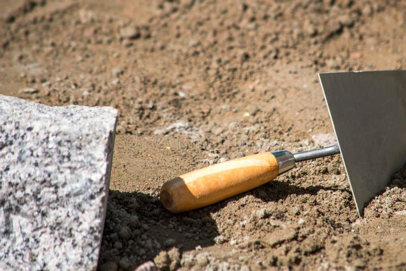 Spatel med ett trähandtag i sanden med ett stycke av granit arkivbild