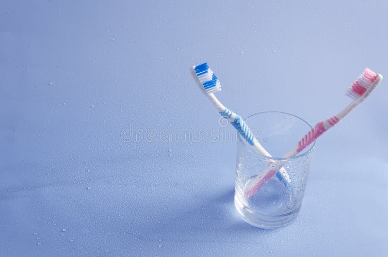 Spazzolini da denti blu e rosa, tazza di vetro sui precedenti blu Spazio vuoto per progettazione fotografia stock Spazzolini da denti blu e rosa, tazza di vetro sui precedenti blu Spazio vuoto per progettazione fotografia stock
