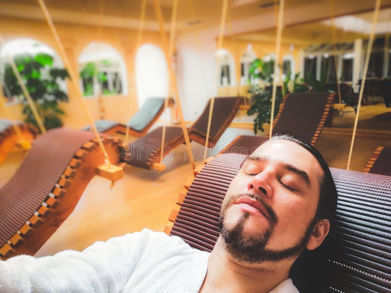 Man in spa relax area on suspended deck chair alone in silence with eyes closed and bathrobe . Man in spa relax area on suspended deck chair alone in silence with eyes closed and bathrobe .