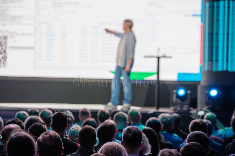 Speaker making a presentation to a large audience at a business conference. The background features a large screen with data. Presenting speaker stock images, royalty-free photos and pictures