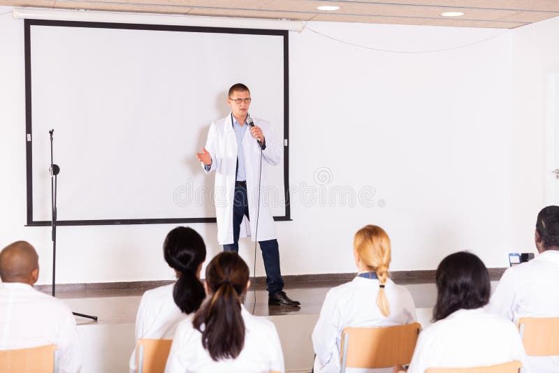 Speaker in white coat giving presentation at medical conference stock photography