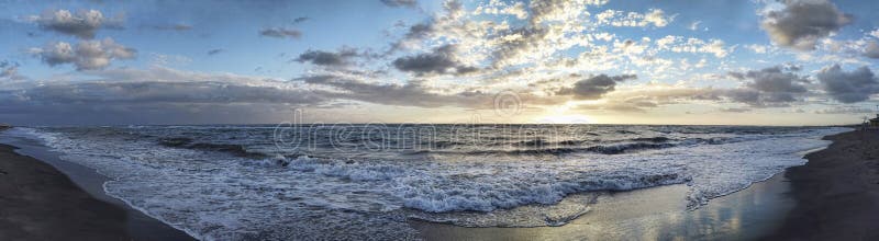 Spectacular panoramic sunset on the Roman coast in Ostia Lido with waves breaking on the shore and blue and golden sky spreads a royalty free stock photo Spectacular panoramic sunset on the Roman coast in Ostia Lido with waves breaking on the shore and blue and golden sky spreads a royalty free stock photo