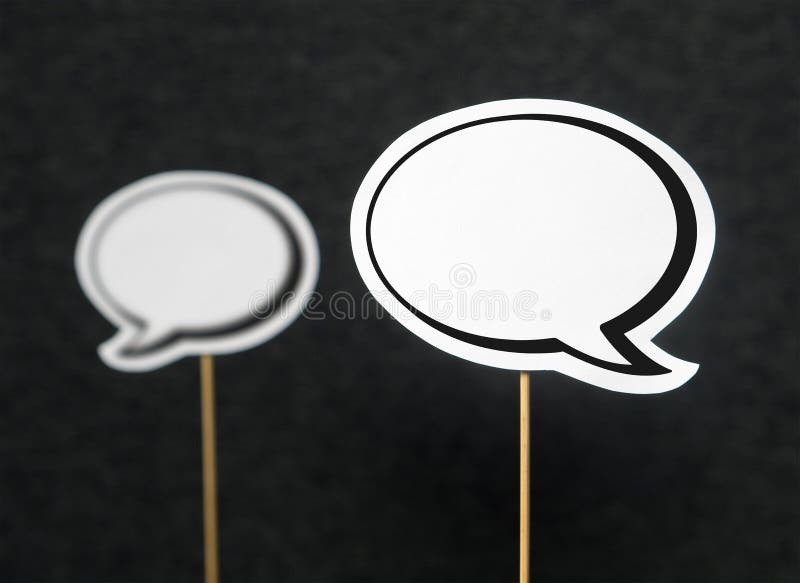 2 blank speech bubbles on a dark black background. The other speech balloon blurred. Chat bubble cut from paper with wooden stick. Discussion, protest and commenting concept with copy space for text. 2 blank speech bubbles on a dark black background. The other speech balloon blurred. Chat bubble cut from paper with wooden stick. Discussion, protest and commenting concept with copy space for text.