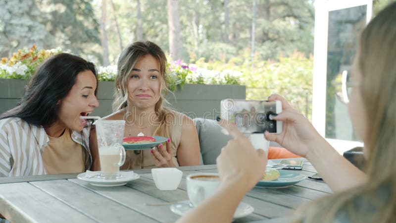 Speelse meisjes vrienden die voor een smartphonecamera pleiten en die plezier hebben in een straatcafé in de zomer