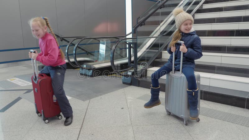 Speelse meisjestiener die op koffer in luchthaven op roltrapachtergrond berijden