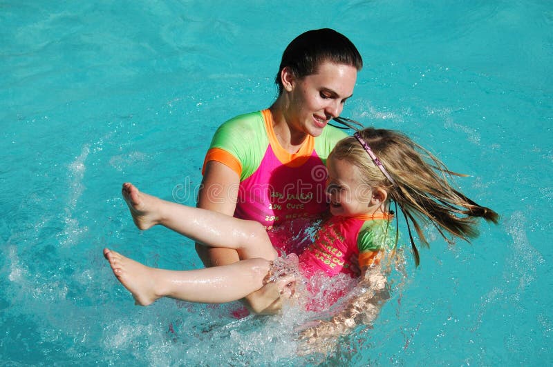 A beautiful brunette young teenager and a pretty blond caucasian white girl child with happy smiling expression in their faces having great fun while playing together turn around in the swimming pool outdoors in the summer holidays. A beautiful brunette young teenager and a pretty blond caucasian white girl child with happy smiling expression in their faces having great fun while playing together turn around in the swimming pool outdoors in the summer holidays