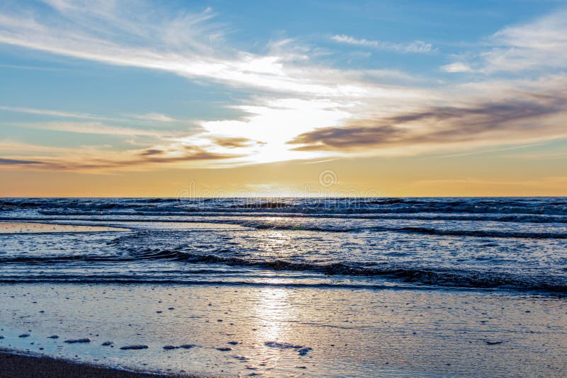 Spiaggia di sabbia con l'orizzonte senza fine ed onde spumose nell'ambito del tramonto luminoso con i colori gialli e nuvole sopr fotografia stock libera da diritti Spiaggia di sabbia con l'orizzonte senza fine ed onde spumose nell'ambito del tramonto luminoso con i colori gialli e nuvole sopr fotografia stock libera da diritti