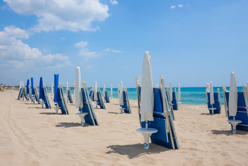 Spiaggia di sabbia con le chaise-lounge blu del sole nel giorno di estate immagini stock Spiaggia di sabbia con le chaise-lounge blu del sole nel giorno di estate immagini stock