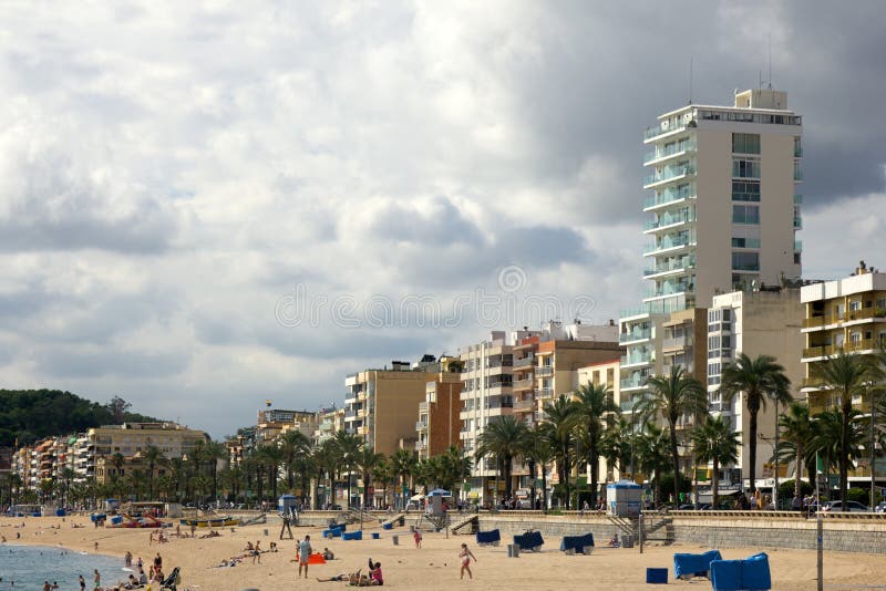 Spain, Lloret de Mar - October 2, 2017: tourist beach with palm trees hotels and vacationers in Mediterranean low season. Spain, Lloret de Mar - October 2, 2017: tourist beach with palm trees hotels and vacationers in Mediterranean low season