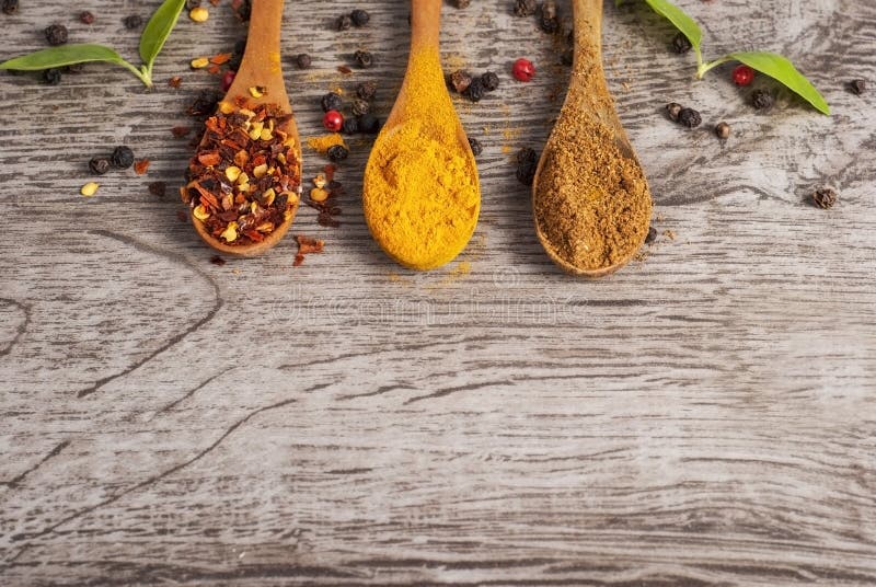 Spices in wooden spoons on wooden background