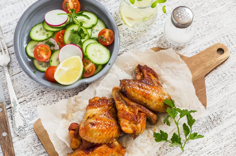 Spicy chicken wings and fresh vegetable salad on wooden white background