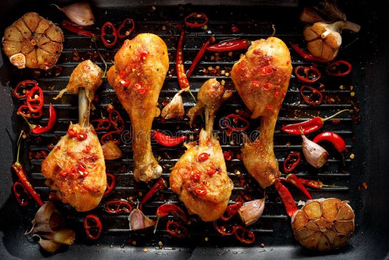 Spicy grilled chicken legs, drumsticks with the addition of chili peppers, garlic and herbs on the grill plate, top view.