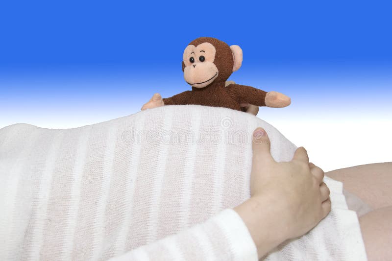 Toy stuffed monkey peeks over striped belly of 38-weeks pregnant young woman. Toy stuffed monkey peeks over striped belly of 38-weeks pregnant young woman