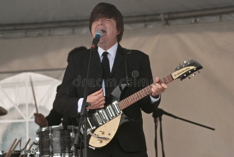 A john lennon impersonator playing guitar on stage. A john lennon impersonator playing guitar on stage