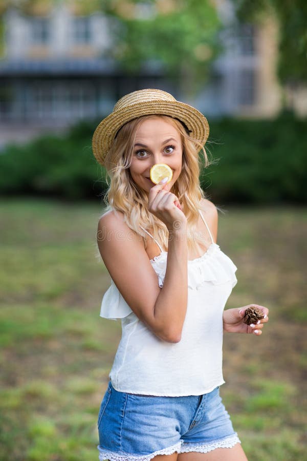 Spielerische junge Frau auf einem Gartenhintergrund Ein frohes Mädchen in einem Hut Mädchen mit einer Zitrone Exotische Diäten Ge lizenzfreies stockfoto Spielerische junge Frau auf einem Gartenhintergrund Ein frohes Mädchen in einem Hut Mädchen mit einer Zitrone Exotische Diäten Ge lizenzfreies stockfoto