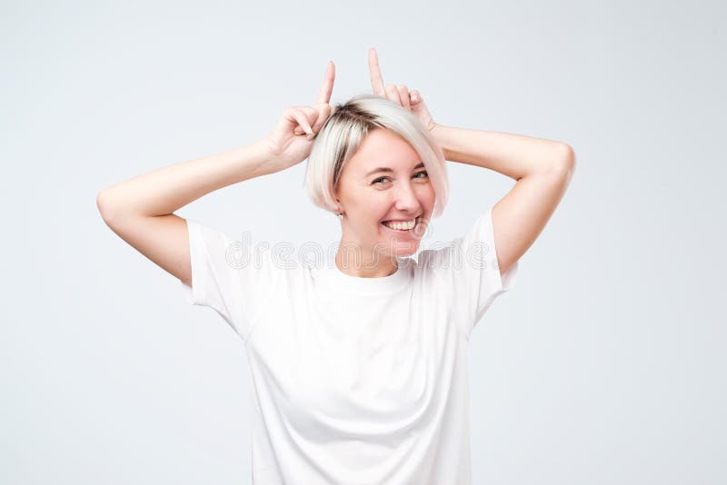 Spielerisches jugendlich Mädchen mit dem farbigen Frisurbehandlungsweißt-shirt, das Hörner zeigt stockfotos Spielerisches jugendlich Mädchen mit dem farbigen Frisurbehandlungsweißt-shirt, das Hörner zeigt stockfotos