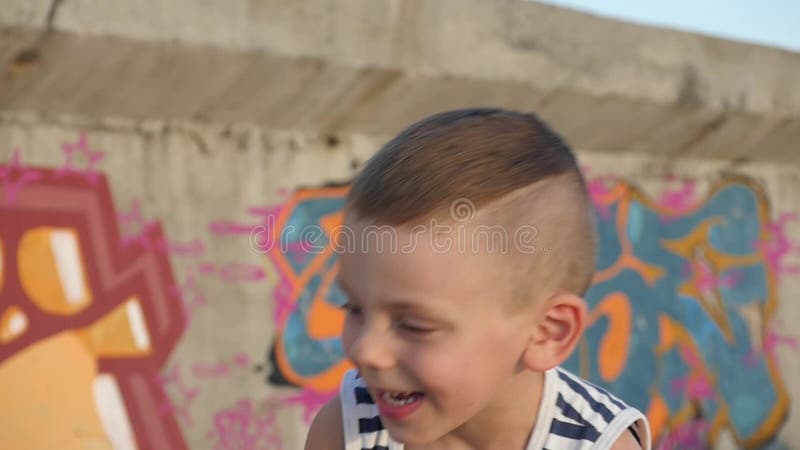 Spielerisches Kleinkind in gestreiftem Hemd nettes Lächeln auf Hintergrundwand mit Graffiti stock video Spielerisches Kleinkind in gestreiftem Hemd nettes Lächeln auf Hintergrundwand mit Graffiti stock video
