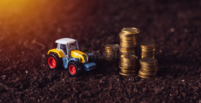 Spielzeug des landwirtschaftlichen Traktors und goldene Münzen auf fruchtbarem Boden landen lizenzfreie stockfotografie Spielzeug des landwirtschaftlichen Traktors und goldene Münzen auf fruchtbarem Boden landen lizenzfreie stockfotografie