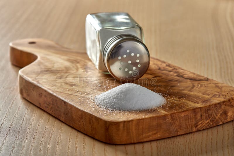 Spilled salt and a salt shaker on a cutting board made from olive wood stock image