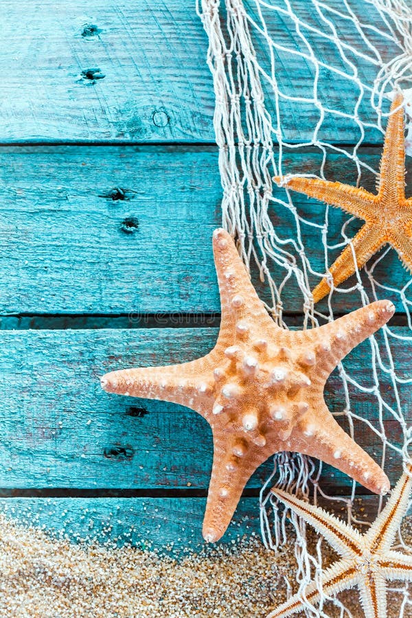 Colorful oceanic background with a marine still life of spiny starfish hanging on diamond mesh fish net on weathered rustic turquoise painted boards with copyspace and beach sand. Colorful oceanic background with a marine still life of spiny starfish hanging on diamond mesh fish net on weathered rustic turquoise painted boards with copyspace and beach sand