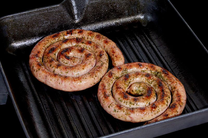Spiral Sausages on a Grill Pan on a Dark Background. Stock Photo