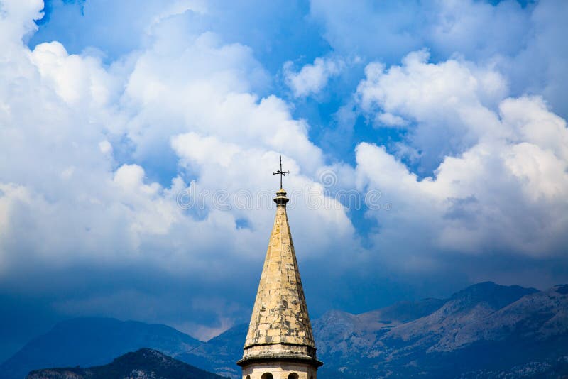 Spire of medieval catholic cathedral on background of stormy sky, dramatic clouds and mountain ranges. Saint Ivan Church in old to