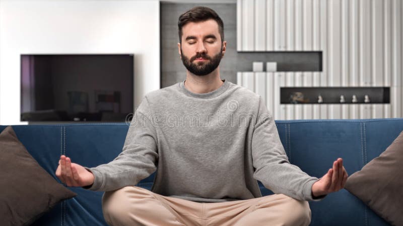 Spirituel homme méditation yoga lotus position mains namaste assis sur le canapé à la maison intérieur