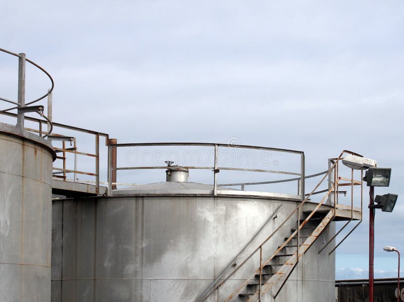 Spitze von großen alten silbernen industriellen Stahlsammelbehältern mit verrostender Treppe und Gehweg der Regelventile gegen ei stockbilder Spitze von großen alten silbernen industriellen Stahlsammelbehältern mit verrostender Treppe und Gehweg der Regelventile gegen ei stockbilder