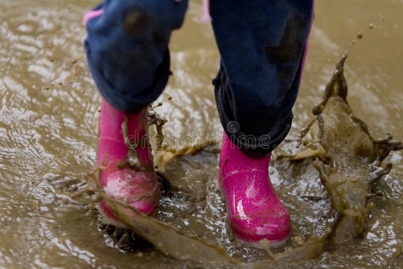 A little girl's pink boots splashing in a muddy puddle. A little girl's pink boots splashing in a muddy puddle