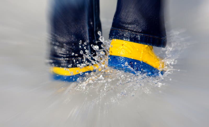 Pair of yellow boots splashing water in puddle with zoom. Pair of yellow boots splashing water in puddle with zoom