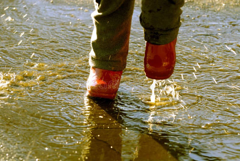 Detail of little girl splashing in puddle with red rain boots. Detail of little girl splashing in puddle with red rain boots
