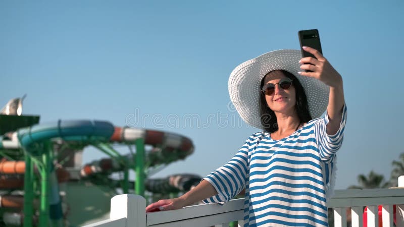 Spokojna, turystyczna młoda kobieta uśmiechająca się biorąc selfie w luksusowym kurorcie aquapark sky tło