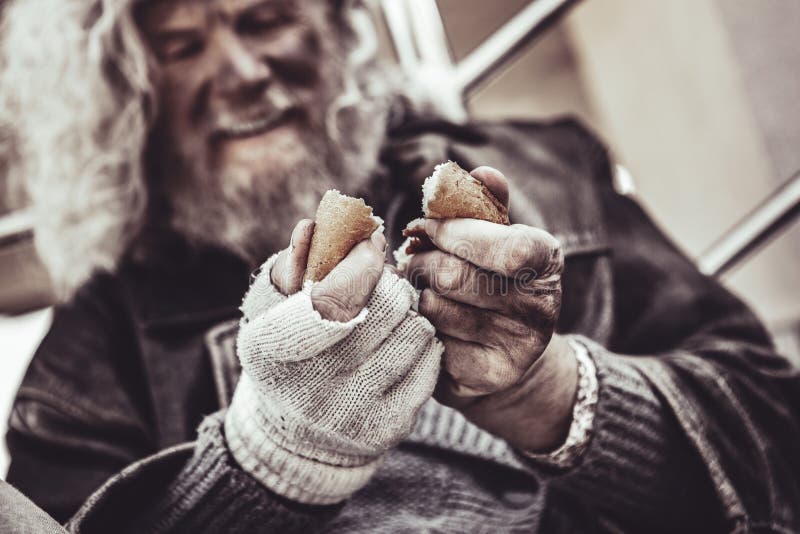 Tasty treat. Calm almsman sincerely sharing piece of bun with another homeless friend. Tasty treat. Calm almsman sincerely sharing piece of bun with another homeless friend.