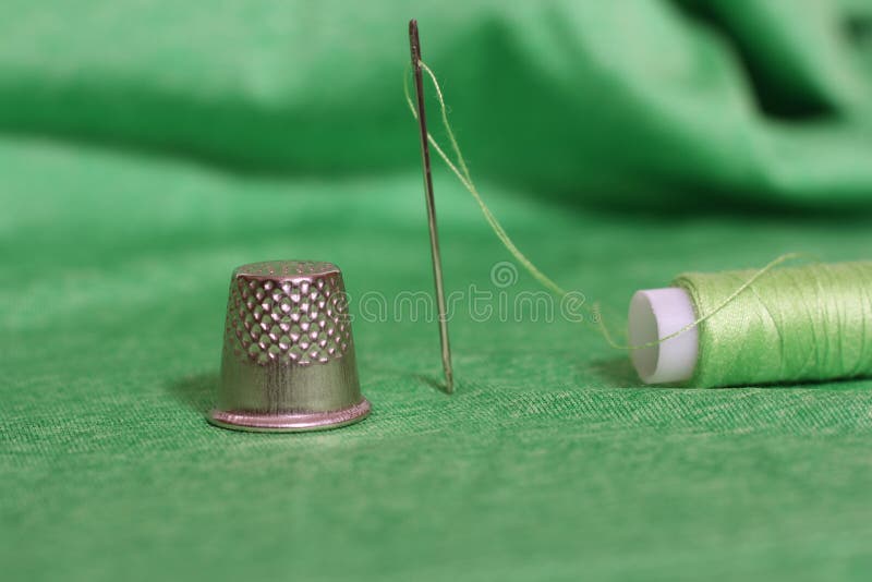 Spool of Green Thread, Thimble and Needle on Green Fabric Stock Photo