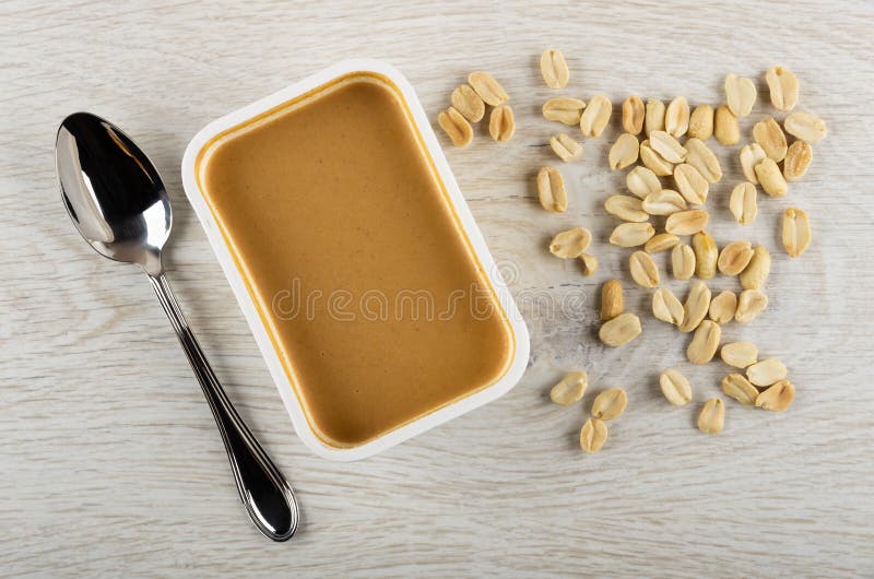 Spoon, Container with Peanut Butter, Fried Peanut on Table. Top View