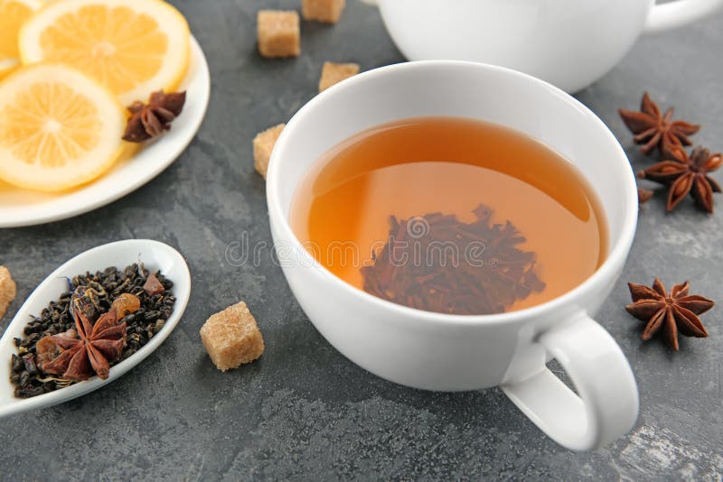 Spoon with dry green tea leaves and cup of aromatic beverage on table