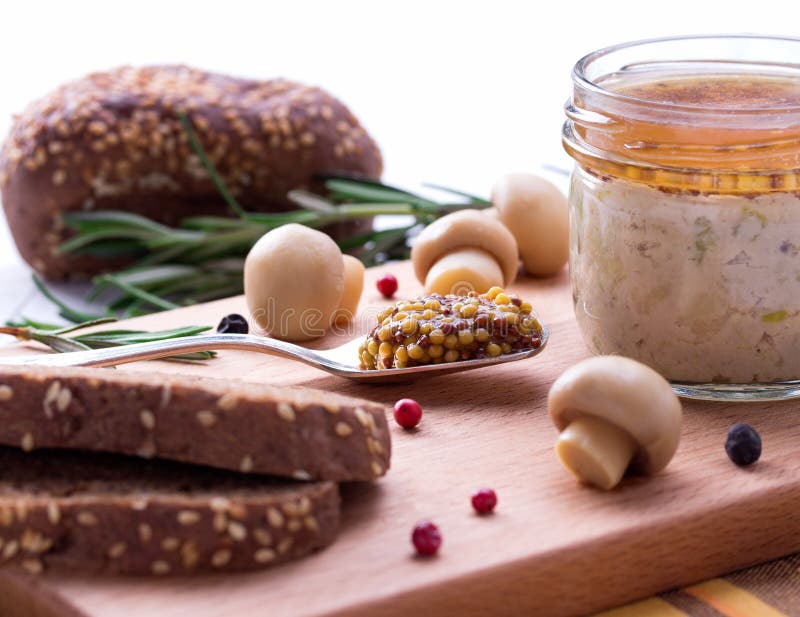 Spoon full of french mustard with chicken pate in jar and sliced bread.