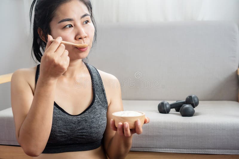 Sport asiatique fille manger yaourt après la forme physique et l'exercice à la maison assis à côté de haltères se sentir frais et image stock