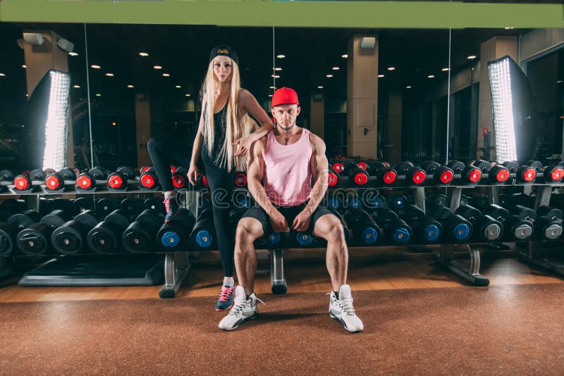 Sport, bodybuilding, tyngdlyftning, livsstil och folkbegrepp - ungt härligt par i stilfull kläder som sitter a arkivbild Sport, bodybuilding, tyngdlyftning, livsstil och folkbegrepp - ungt härligt par i stilfull kläder som sitter a arkivbild