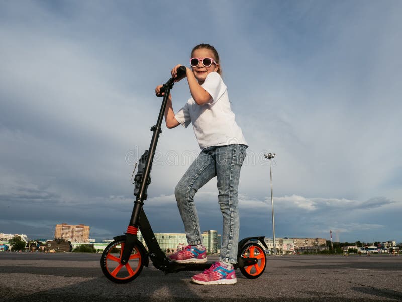 Sport de rue : Fille heureuse en montant un scooter de coup-de-pied sur le trottoir et les magmas image stock Sport de rue : Fille heureuse en montant un scooter de coup-de-pied sur le trottoir et les magmas image stock