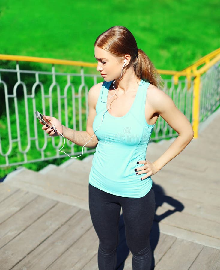 Sport en fitness concept - de mooie jonge vrouw luistert aan muziek en het gebruiken van smartphone in stad stock fotografie Sport en fitness concept - de mooie jonge vrouw luistert aan muziek en het gebruiken van smartphone in stad stock fotografie