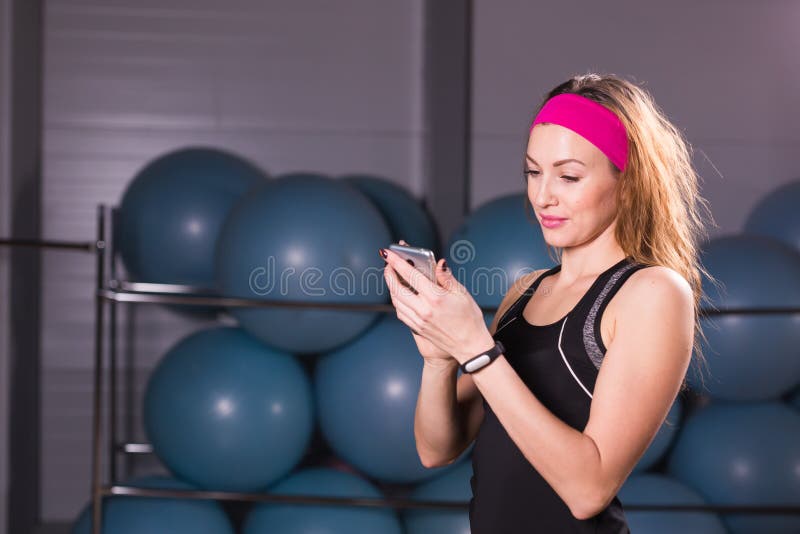 Sport, fitness, technology and people concept - young woman with activity tracker and smartphone in gym