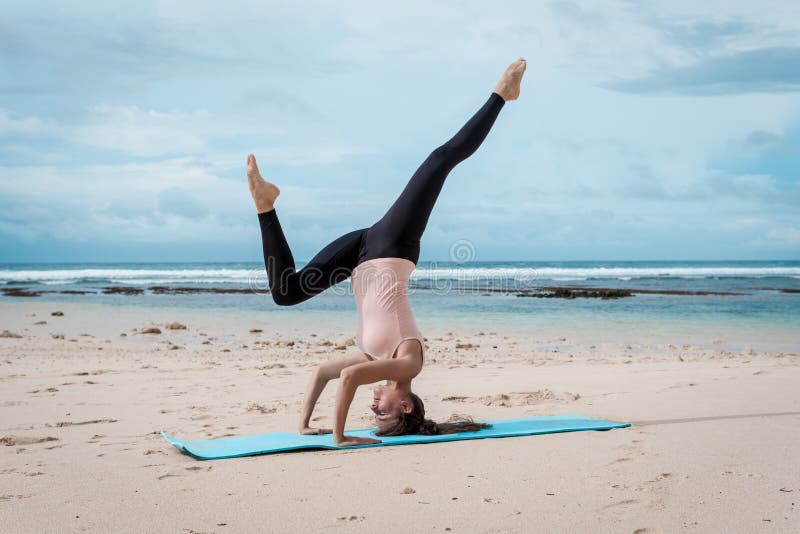 Sport, fitness, yoga, people and health concept - young woman doing headstand exercise on beach background stock images Sport, fitness, yoga, people and health concept - young woman doing headstand exercise on beach background stock images